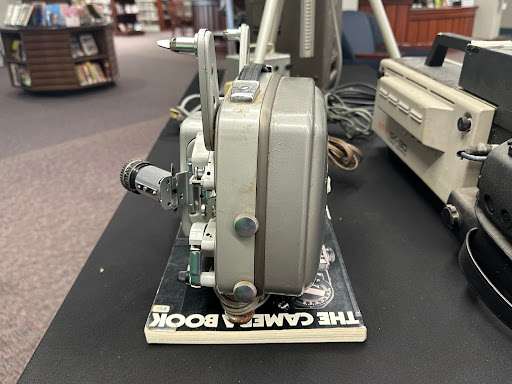 a boxy grey antique camera on top of a book called The Camera Book