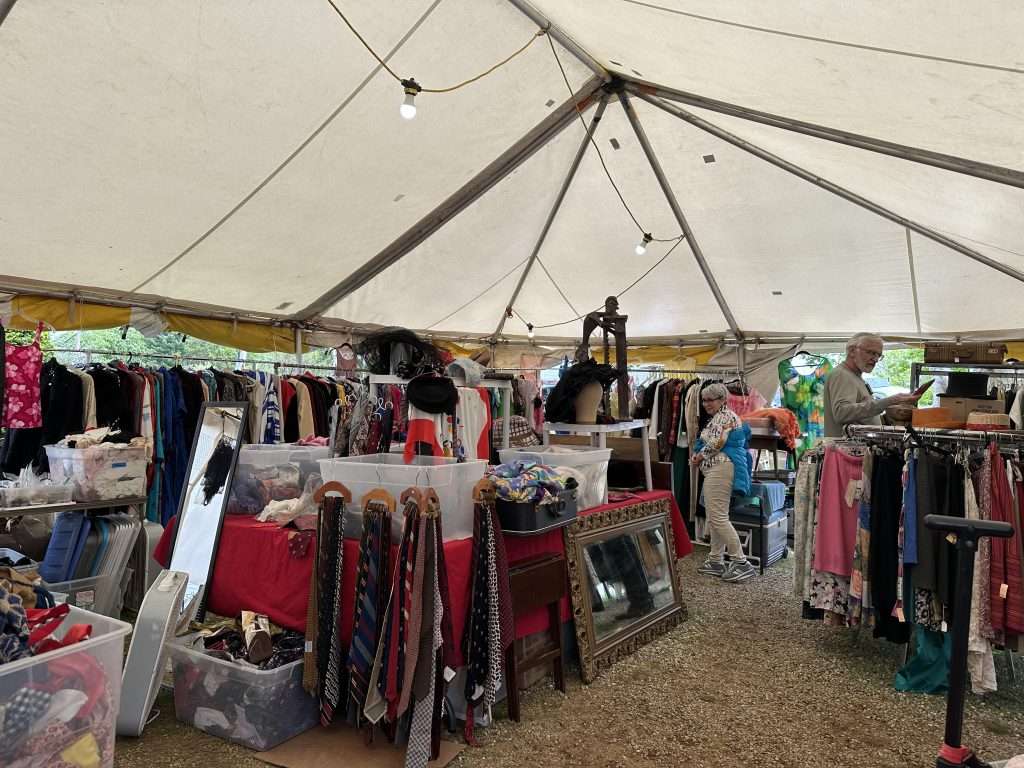 A welcoming-looking, colorful tent filled with antique clothing (shirts, skirts, ties, and more) displayed on racks and tables.