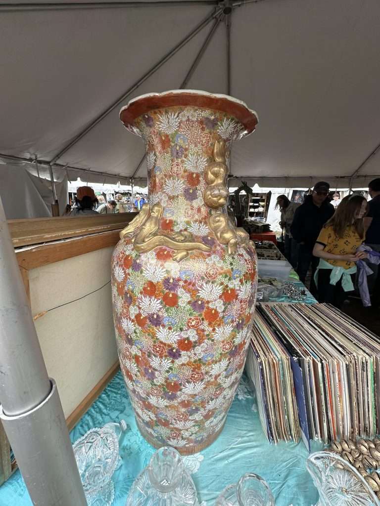 A large vase covered in intricate flowers of many colors, as well as large, 3-D gold decorative shapes