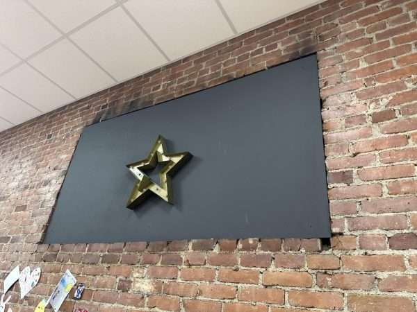 A brick wall with a large black rectangle decoration with a gold star decoration in the center. Where the rectangle meets the wall, there are blackened areas.