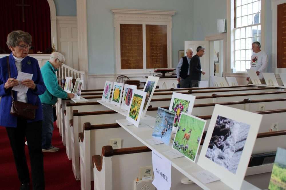 Visitors peruse the entries in the 20 th annual Oldtown Photo Calendar competition at EliotChurch in South Natick on Oct. 19. Winning entries will appear in the 2027 calendar.