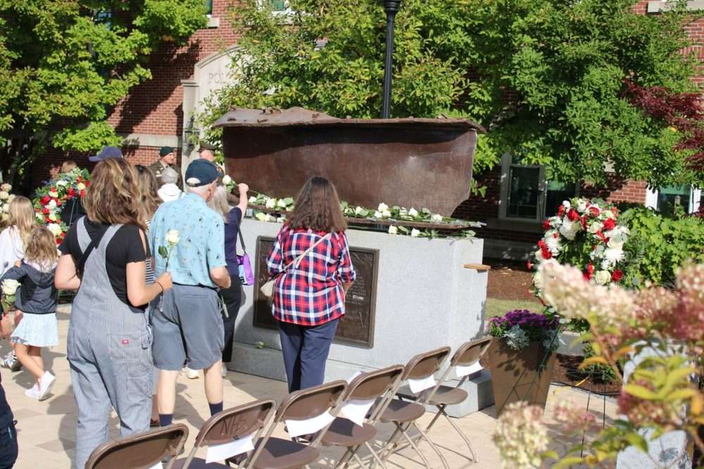 At the conclusion of the town’s observance of the 25 th anniversary of the terrorist attacks on Sept. 11, 2001, attendees placed flowers – donated by TJX, which lost seven employees in the attacks – at the 9/11 memorial. It features a piece of steel from “ground zero” in New York City.